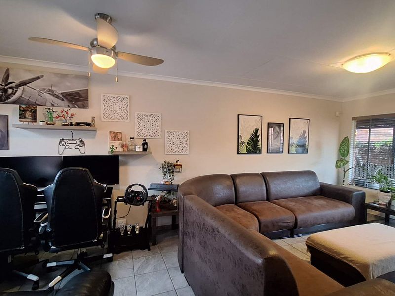 A spacious living room featuring tiled flooring, a ceiling fan, and large windows with blinds, providing a comfortable and functional living space.