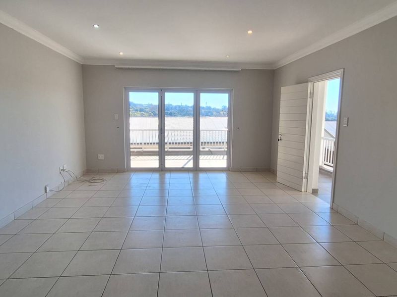 A bright, spacious, and empty living area featuring neutral tiled flooring, recessed downlighting, and large sliding glass doors leading to an outdoor balcony.