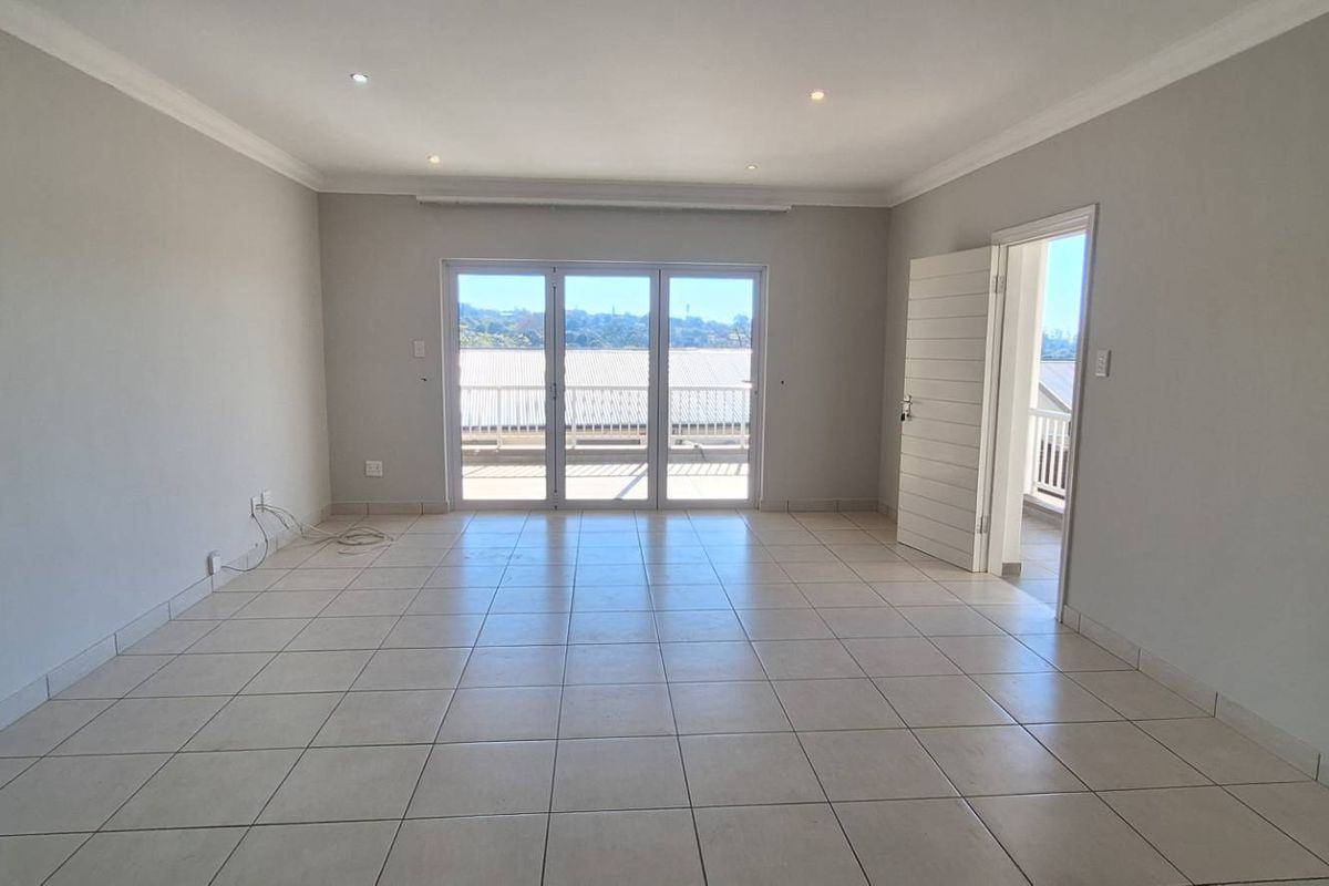 A bright, spacious, and empty living area featuring neutral tiled flooring, recessed lighting, and large sliding glass doors leading to an outdoor balcony.