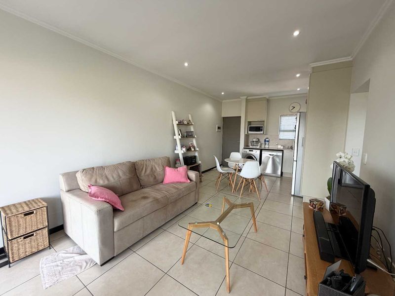 Open-plan living area featuring tiled flooring, recessed lighting, and a compact kitchen space with integrated laundry connections.
