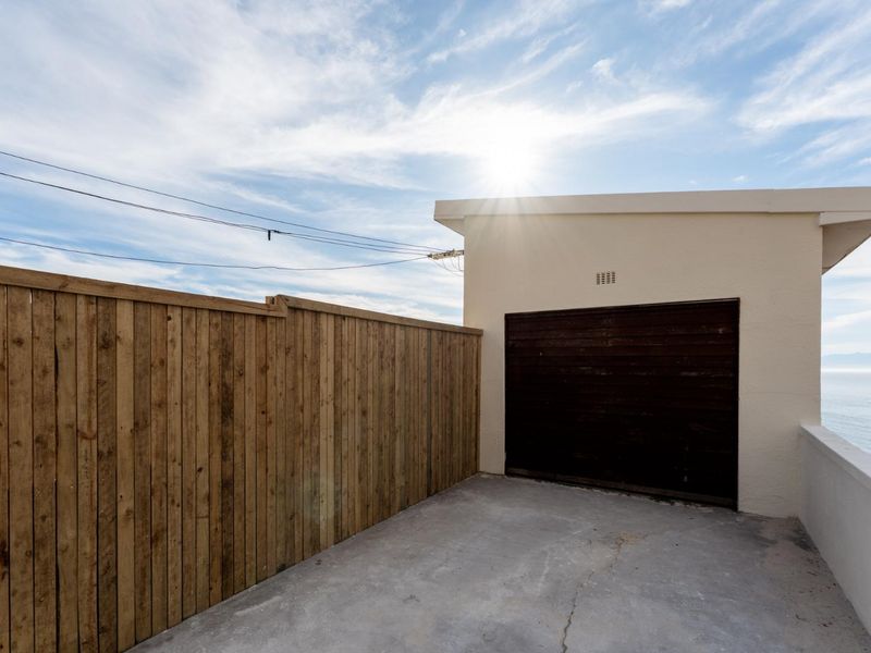 Rear exterior area featuring a concrete driveway, timber fencing, and a garage entrance with a view of the coastline.