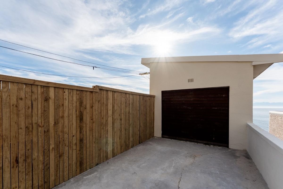 Rear exterior area featuring a concrete driveway, timber fencing, and a garage entrance with a view of the coastline.