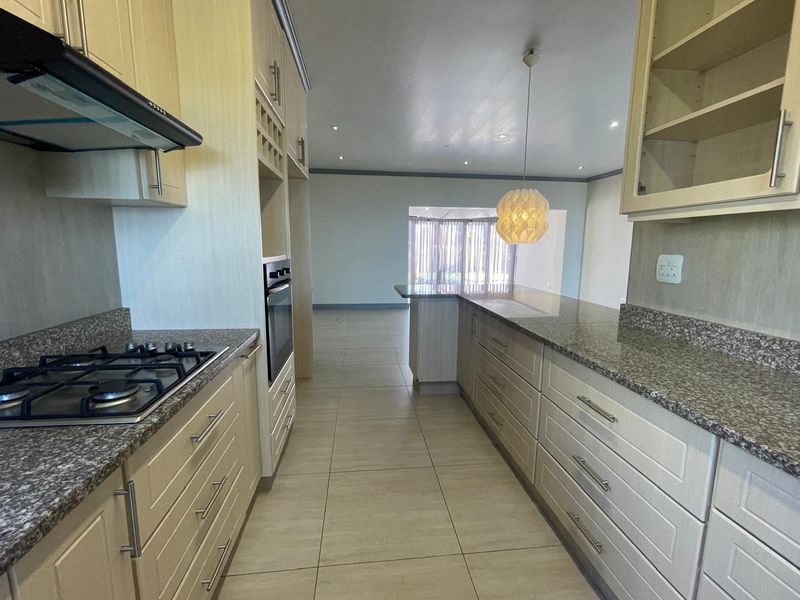 Modern kitchen featuring granite countertops, built-in oven, gas hob, and ample cabinetry, flowing into an open-plan living area with tiled flooring throughout.