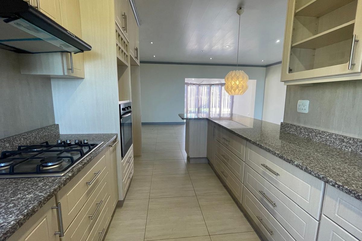 Modern kitchen featuring granite countertops, built-in oven, gas hob, and ample cabinetry, flowing into an open-plan living area with tiled flooring throughout.