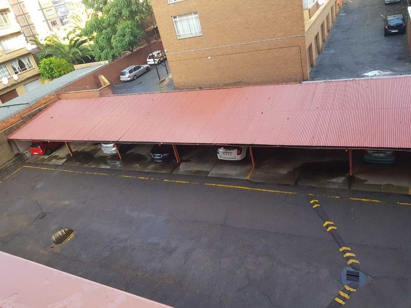 An elevated view of an outdoor covered parking area with corrugated metal roofing and marked asphalt bays.