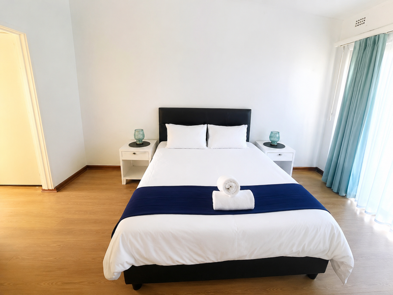A bright and clean bedroom featuring light wood-look laminate flooring and neutral wall finishes, providing a simple and functional living space.
