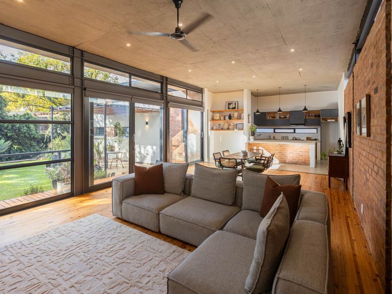 Spacious open-plan living and kitchen area featuring exposed concrete ceilings, brick feature walls, timber floors, and large glass doors opening to the garden.