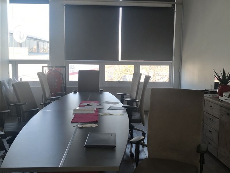 A functional office space featuring large windows with roller blinds, a suspended ceiling, and laminate flooring, suitable for a professional work environment.