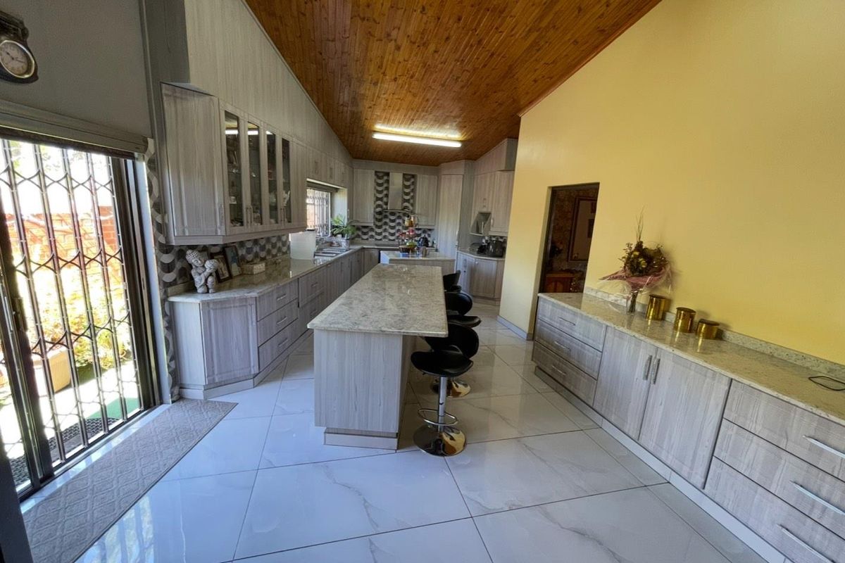 Spacious kitchen featuring modern cabinetry, stone countertops, a central island, and high-gloss tiled flooring under a vaulted timber ceiling.