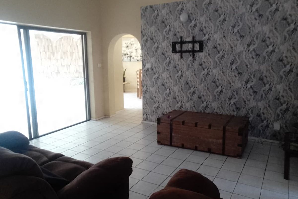 A living room featuring tiled flooring, a feature wall with patterned wallpaper, and sliding glass doors providing access to the outdoor area.