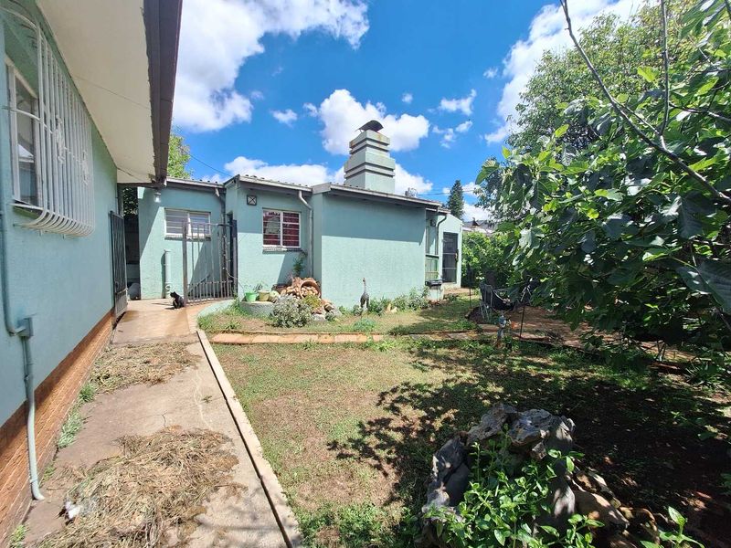 Rear exterior view of the property featuring a garden area, concrete pathways, and a prominent chimney stack against a clear blue sky.