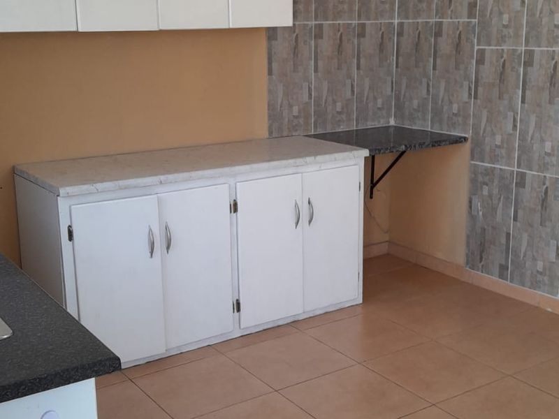 A functional kitchen area featuring white built-in cabinetry, tiled splashbacks, and tiled flooring, offering a clean and practical space for culinary activities.