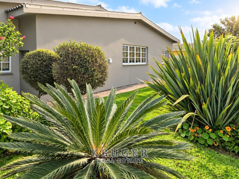 A well-maintained rear exterior view of the house featuring a paved walkway, manicured lawn, and established garden landscaping.