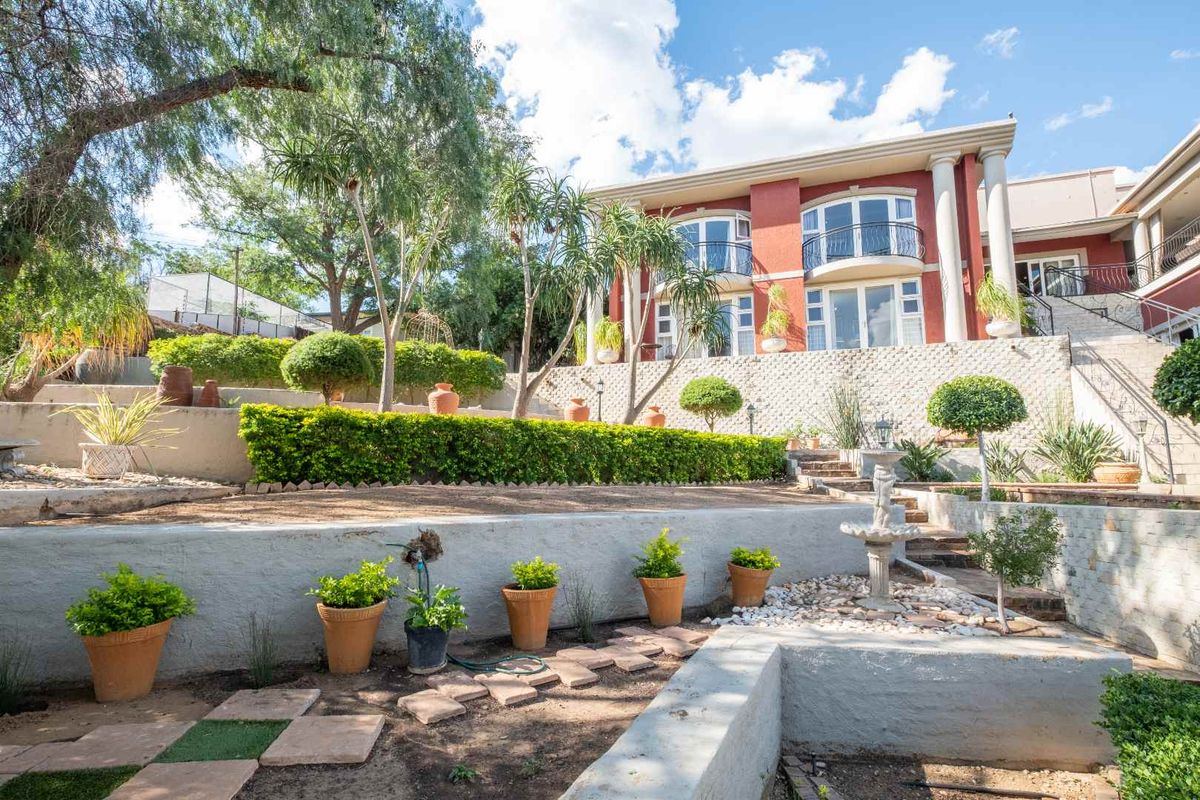 A multi-level terraced garden featuring stone retaining walls, established landscaping, and a rear view of the multi-story residence with balcony access.