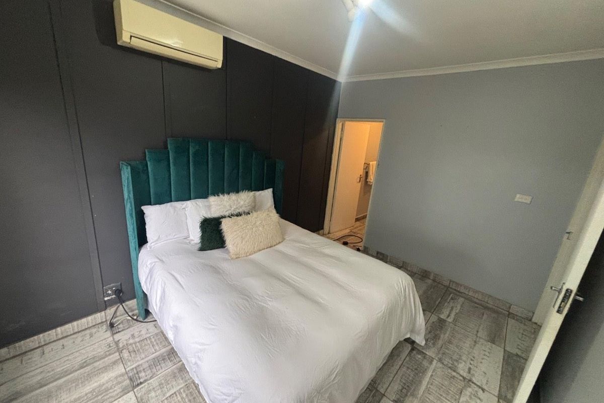 A bedroom featuring tiled flooring, a dark accent wall, and a wall-mounted split-system air conditioner, with an adjoining doorway leading to another room.