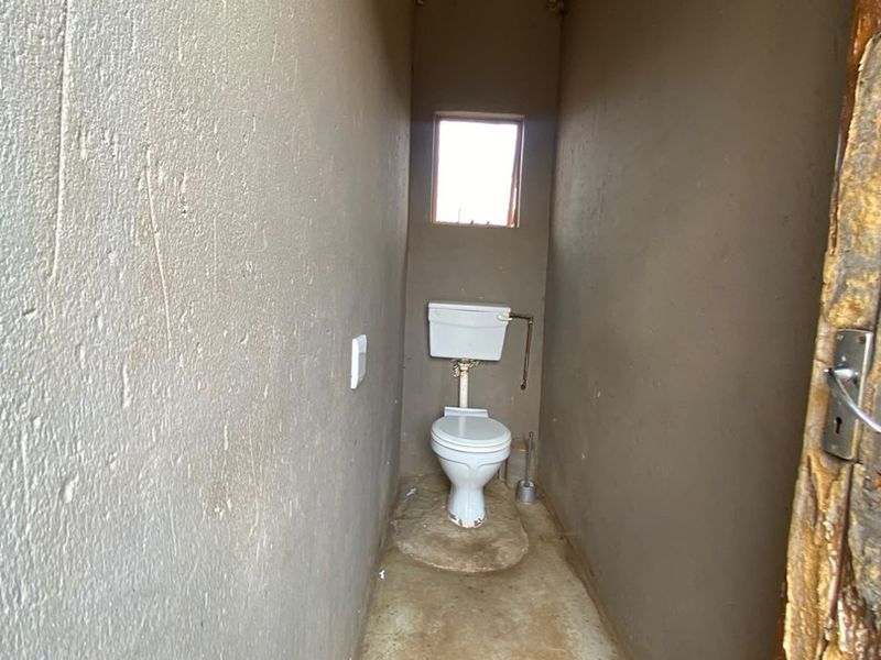 A basic, unfinished bathroom featuring a standard toilet, exposed corrugated metal roofing, and raw concrete flooring.