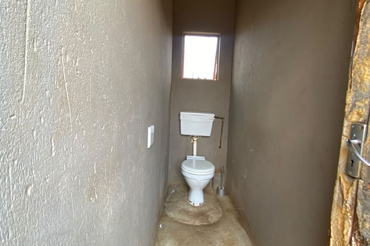 A basic, unfinished bathroom featuring a standard toilet, exposed corrugated metal roofing, and raw concrete flooring.