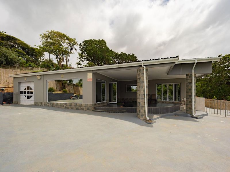 A spacious rear exterior view featuring a large covered patio with stone-clad pillars, extensive glass sliding doors, and a paved driveway area.