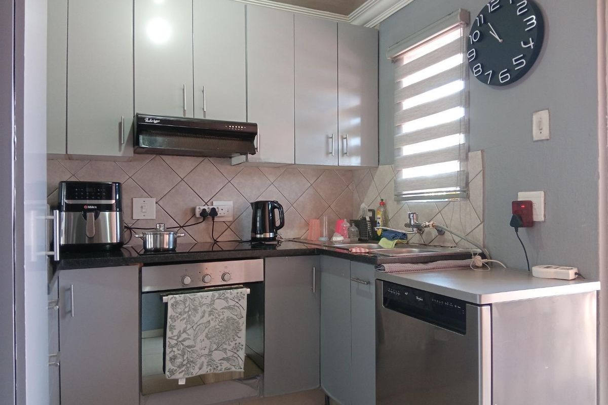 Compact kitchen featuring grey cabinetry, granite countertops, built-in oven, extractor fan, and integrated dishwasher space.