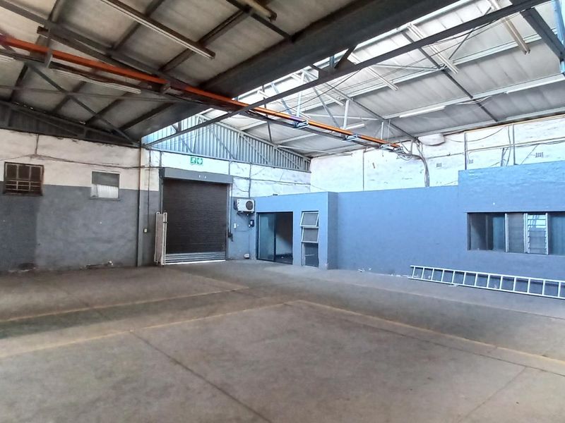 Spacious industrial utility area featuring high ceilings with exposed steel trusses, concrete flooring, and a large roller shutter door for easy access.