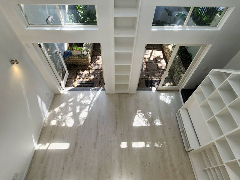 Bright, double-volume living area featuring built-in shelving, light laminate flooring, and dual glass doors opening onto a private courtyard.