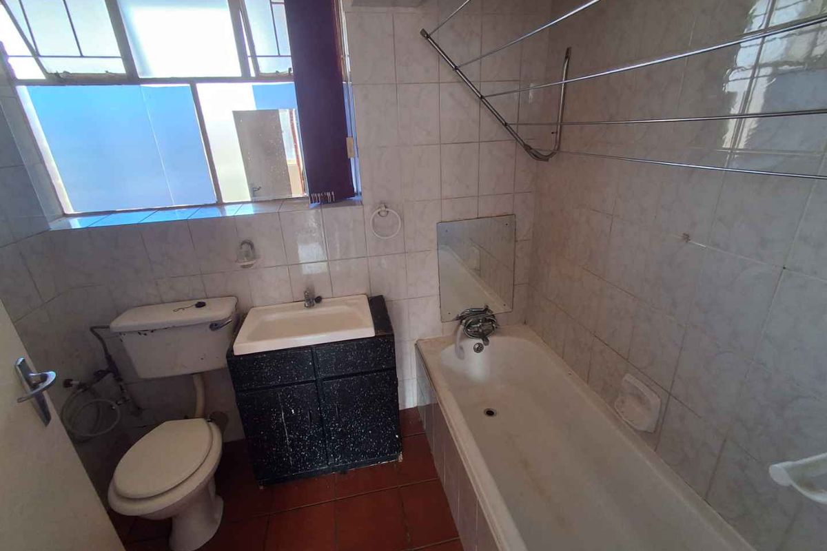 A dated bathroom featuring a standard bathtub, pedestal-style vanity, and toilet, with tiled walls and flooring and a large window for natural light.