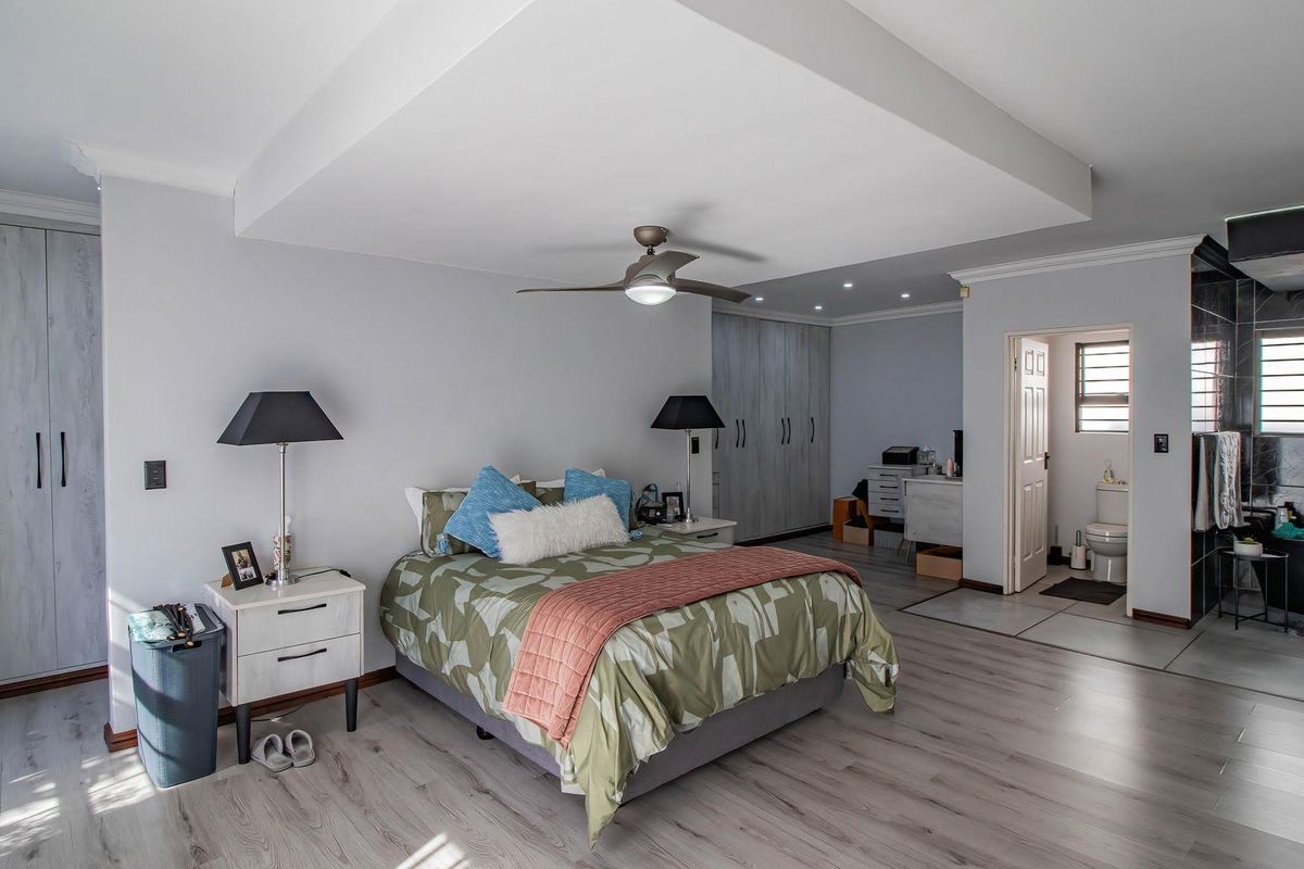 Spacious bedroom featuring modern laminate flooring, built-in cupboards, a ceiling fan, and an integrated en-suite bathroom with tiled finishes.
