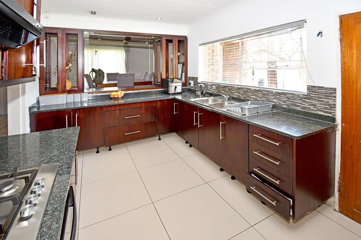 A functional kitchen featuring dark wood cabinetry, granite countertops, a built-in gas hob, and a tiled floor with a serving hatch to the dining area.