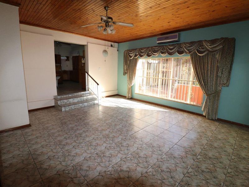 Spacious living area featuring tiled flooring, timber ceiling, and a split-system air conditioner, with a step leading to an adjacent room.