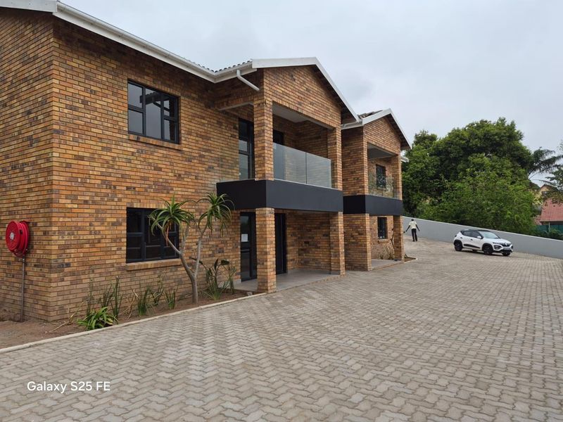 A modern double-story townhouse featuring a face brick exterior, glass-railed balconies, and a neatly paved driveway.