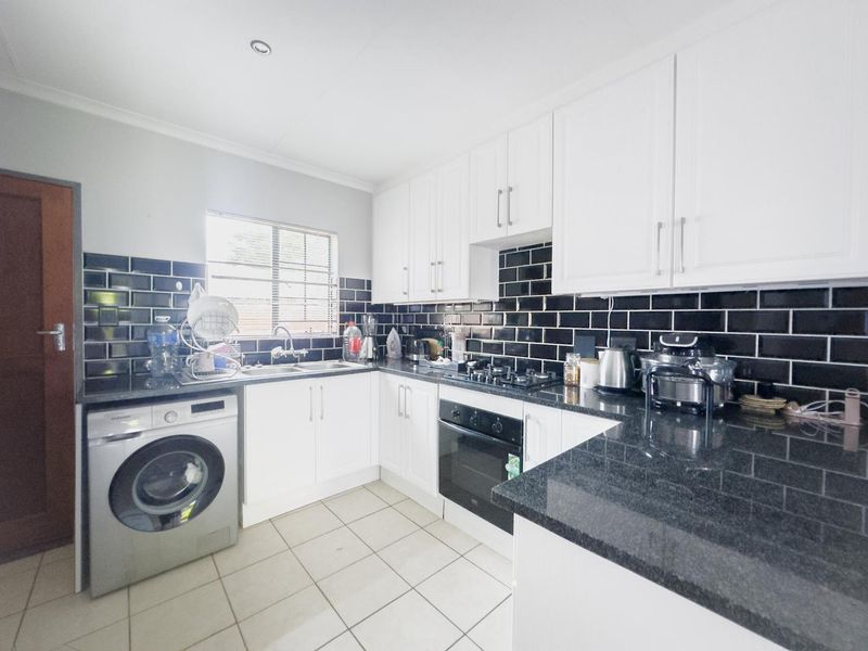A functional kitchen featuring white cabinetry, black granite countertops, a striking black subway tile backsplash, and integrated appliances including a built-in oven and hob.