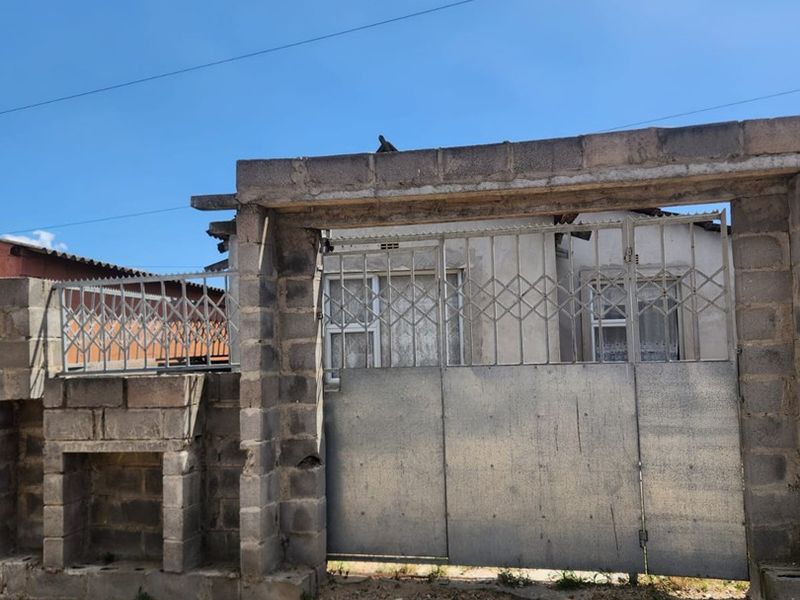 Front view of the property featuring a concrete block boundary wall and a metal security gate entrance.