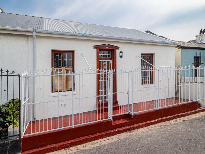 Front facade of a charming cottage featuring a corrugated metal roof, secure gated entrance, and traditional timber window frames.