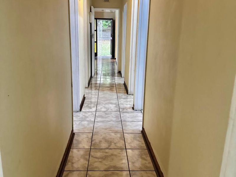 A long, empty residential hallway featuring tiled flooring, textured ceiling, and multiple doorways leading to other rooms.