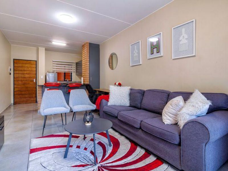 Open plan living area featuring tiled flooring, an exposed brick breakfast bar, and direct access to the kitchen and entrance.