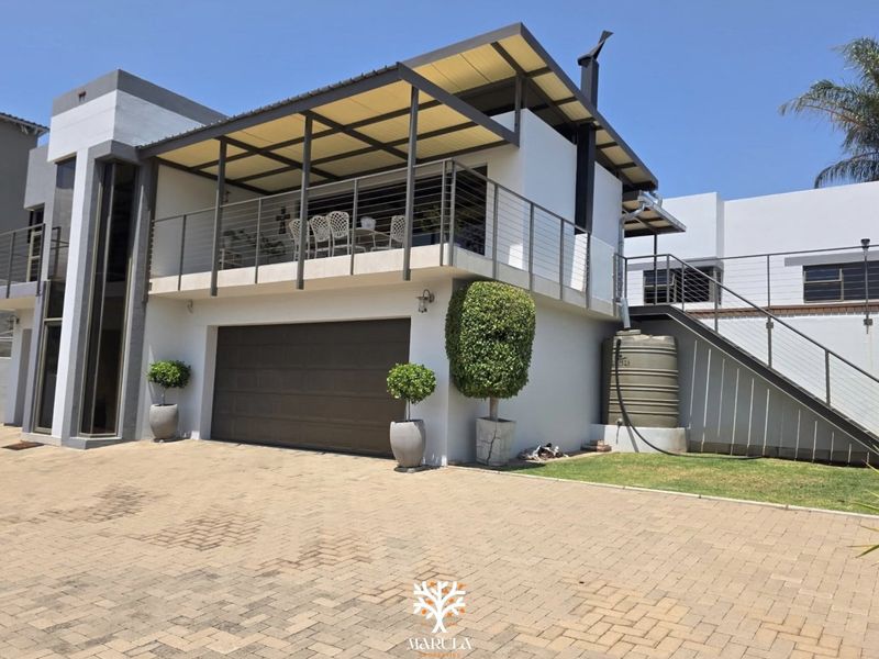 Modern double-story home exterior featuring a paved driveway, integrated double garage, and a spacious covered balcony with steel balustrades.