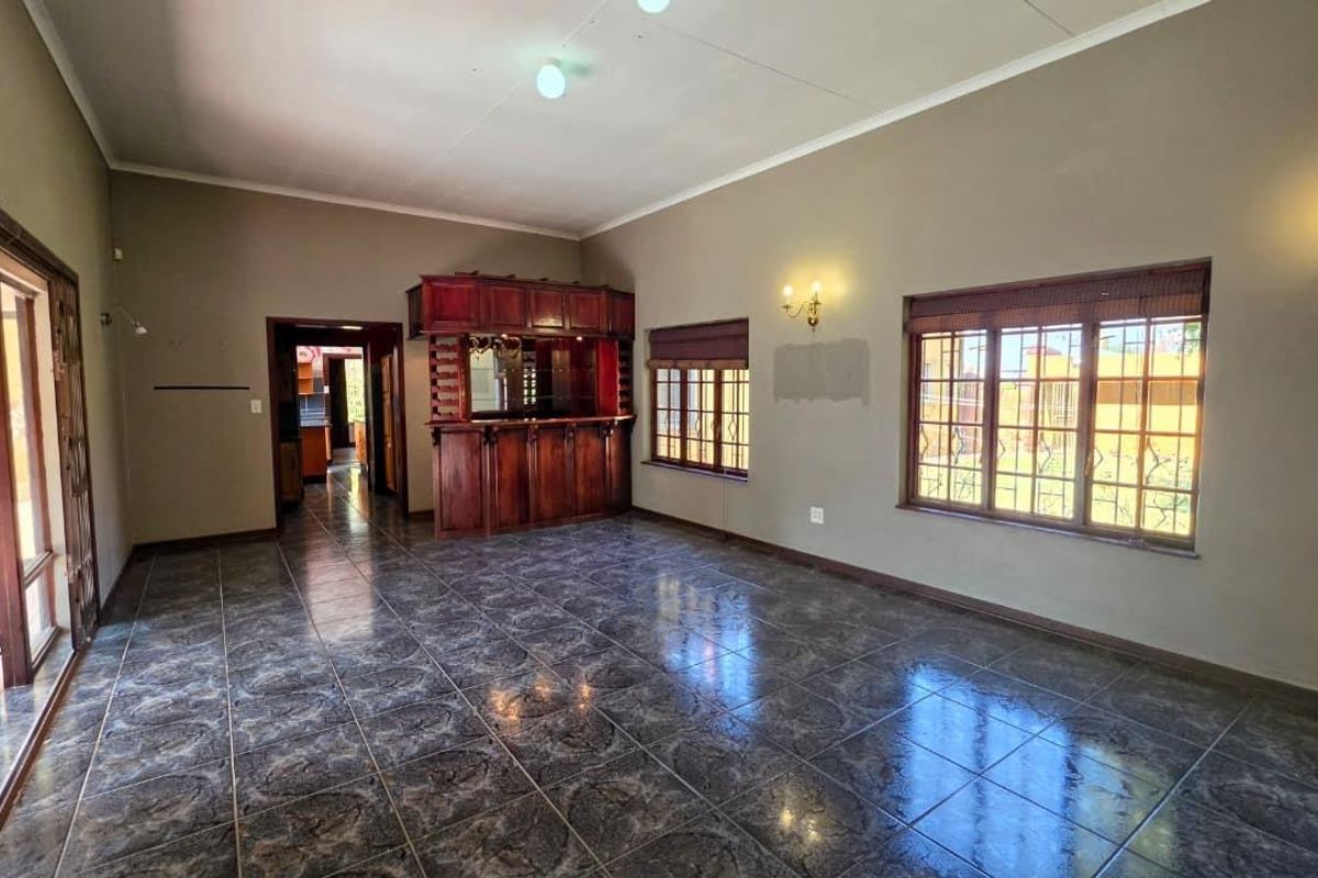 Spacious living area featuring tiled flooring, a built-in wooden bar, and large windows with security bars, offering a versatile space for entertaining.