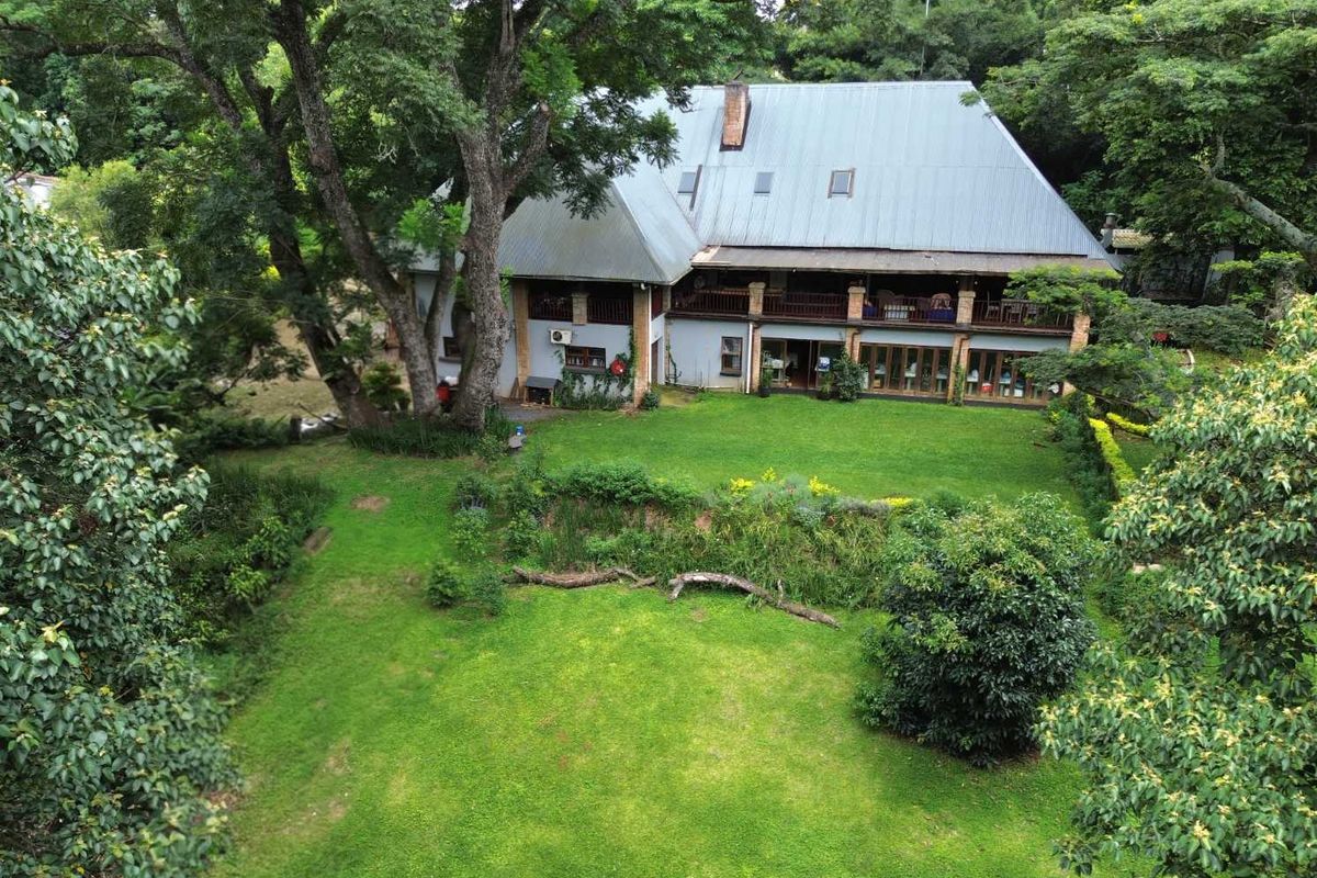 Aerial view of a large residential property featuring a spacious rear garden, mature trees, and a multi-level home with a covered balcony.