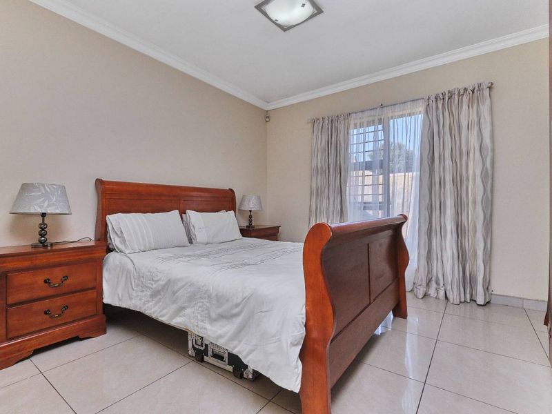 A well-maintained bedroom featuring tiled flooring, a built-in wardrobe, and a window with security bars, offering a functional and comfortable living space.