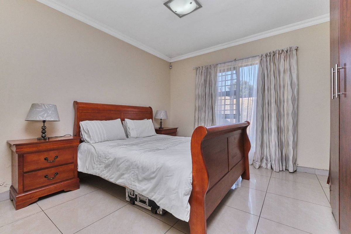 A well-maintained bedroom featuring tiled flooring, a built-in wardrobe, and a window with security bars, offering a functional and comfortable living space.