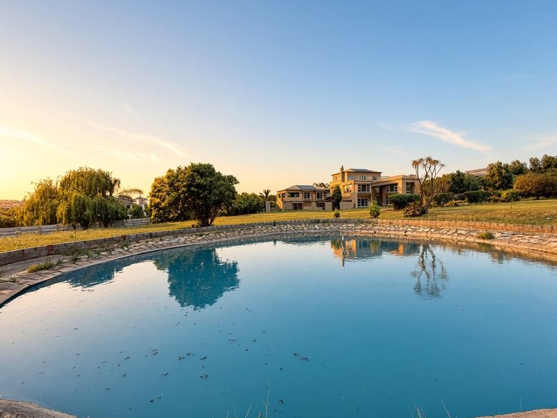 A wide-angle view of a large swimming pool with stone coping, set within a spacious landscaped garden with the main house in the background.