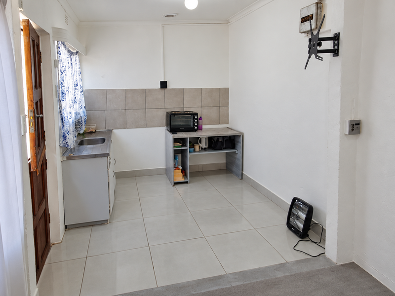 A compact kitchen area featuring tiled flooring, a stainless steel sink, and a tiled backsplash, offering a functional space ready for modernization.
