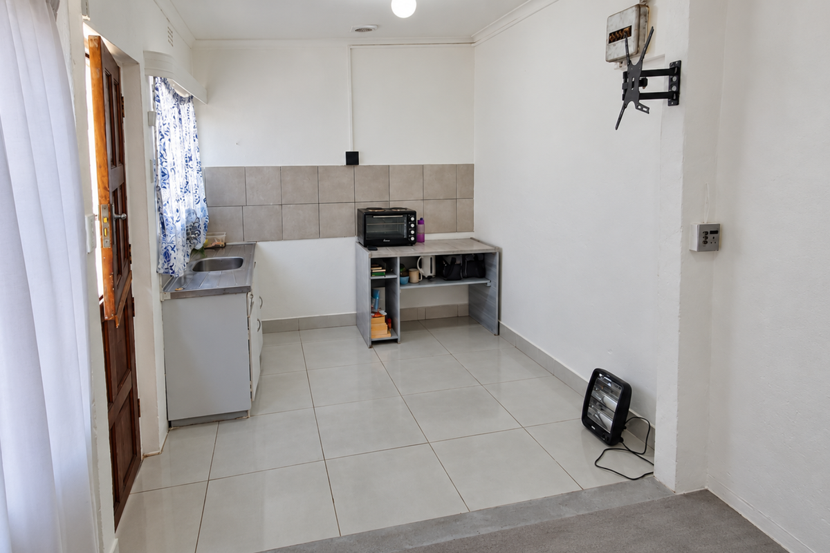 A compact kitchen area featuring tiled flooring, a stainless steel sink, and a tiled backsplash, offering a functional space ready for modernization.