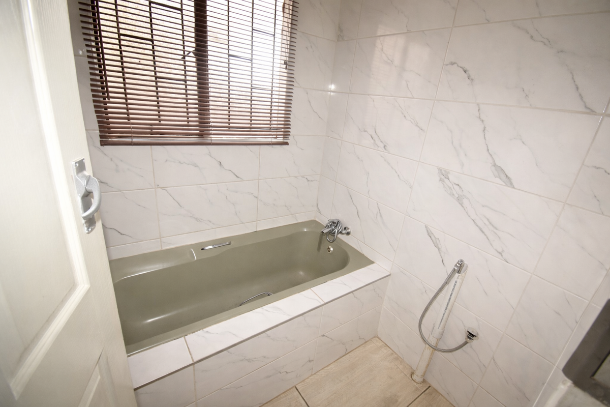 A bathroom featuring a built-in bathtub with marble-look wall tiling, a window with blinds, and a handheld shower attachment.
