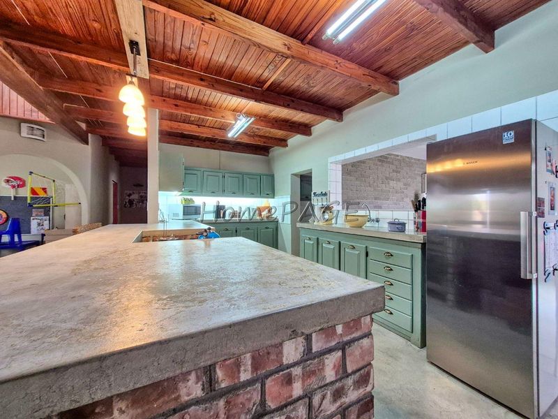 Spacious kitchen featuring a rustic brick island with concrete countertop, exposed timber ceiling beams, and ample built-in cabinetry.