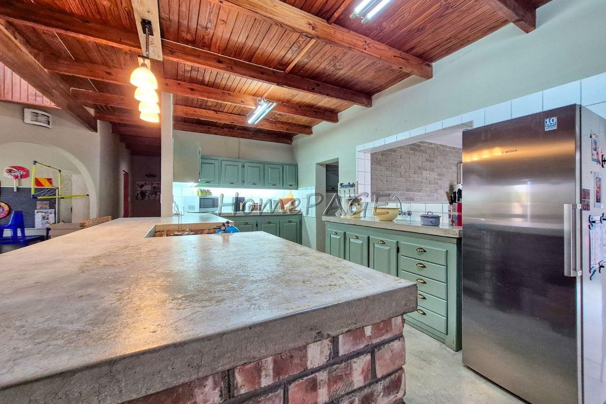 Spacious kitchen featuring a rustic brick island with concrete countertop, exposed timber ceiling beams, and ample built-in cabinetry.
