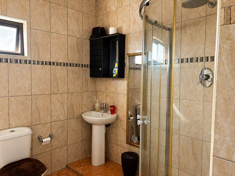 A functional bathroom featuring a pedestal sink, a glass-enclosed shower, and neutral floor-to-ceiling wall tiling.