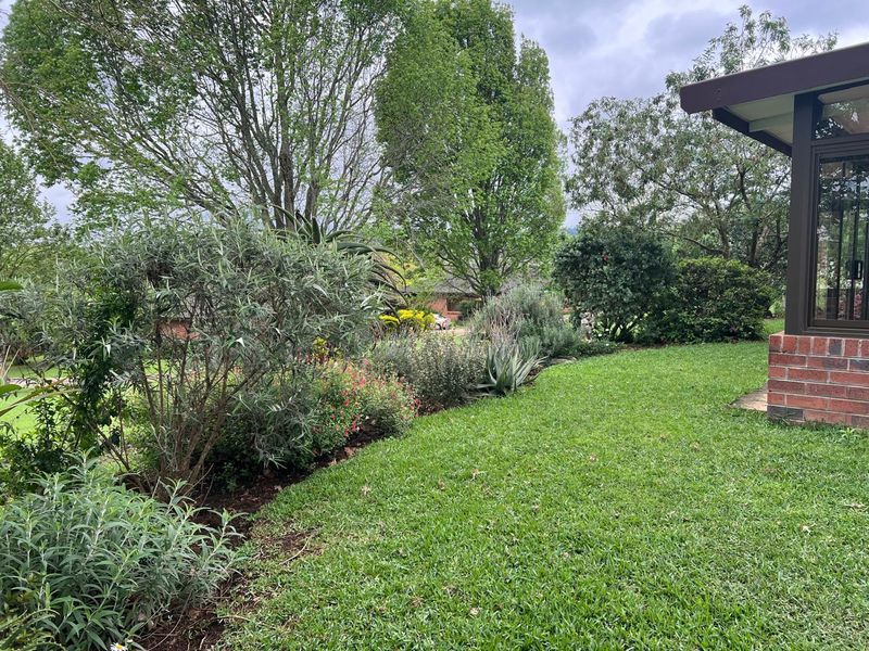 A well-maintained garden area featuring a lush lawn and established shrubbery, adjacent to the brick exterior of the townhouse.