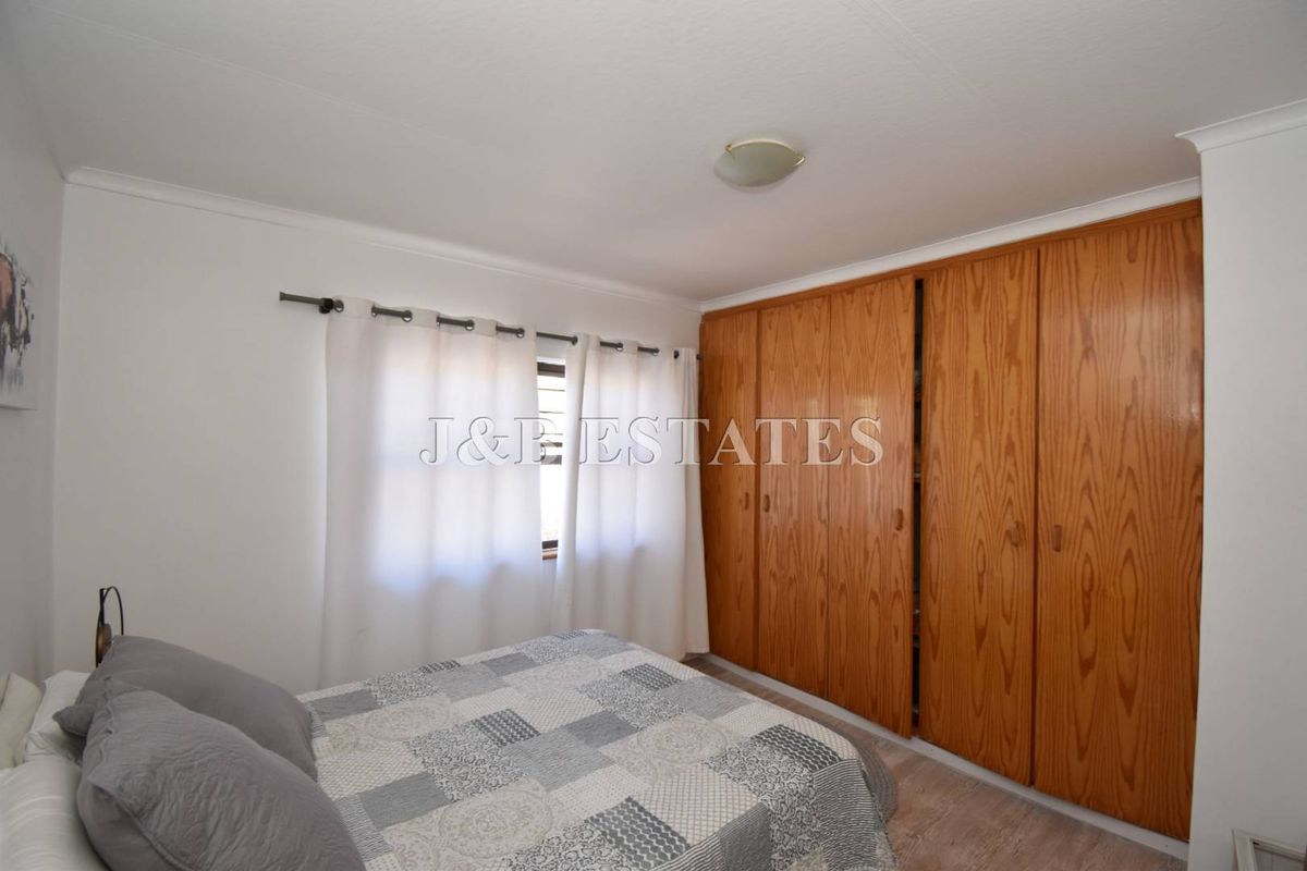 A bedroom featuring built-in wooden wardrobes and a window with curtain rod.