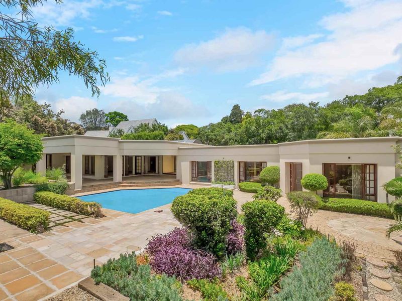Spacious rear exterior featuring a swimming pool, paved patio area, covered terrace, and well-maintained landscaped gardens.